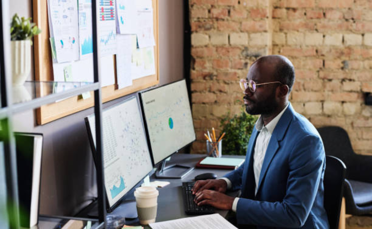 Analyst sitting at table with computer monitors and typing on computer key, he working with charts doing analysis